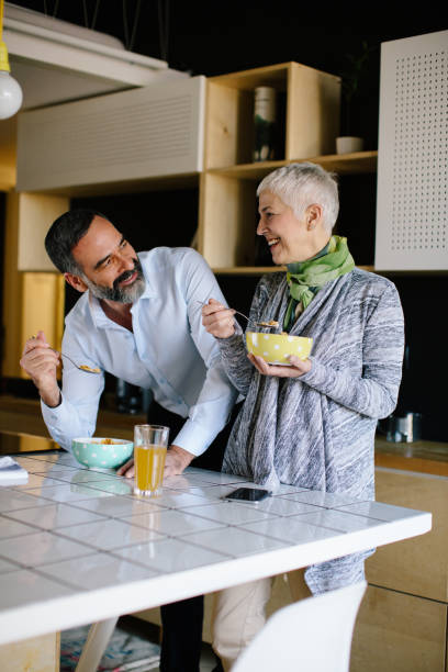 Senior couple in kitchen having breakfast and talking. Shallow DOF. Developed from RAW; retouched with special care and attention; Small amount of grain added for best final impression. 16 bit Adobe RGB color profile.